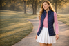 Elegant female golfer walking on a path through the woods wearing a white skort and blue vest
