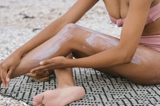 a woman sitting on a towel applying sunscreen