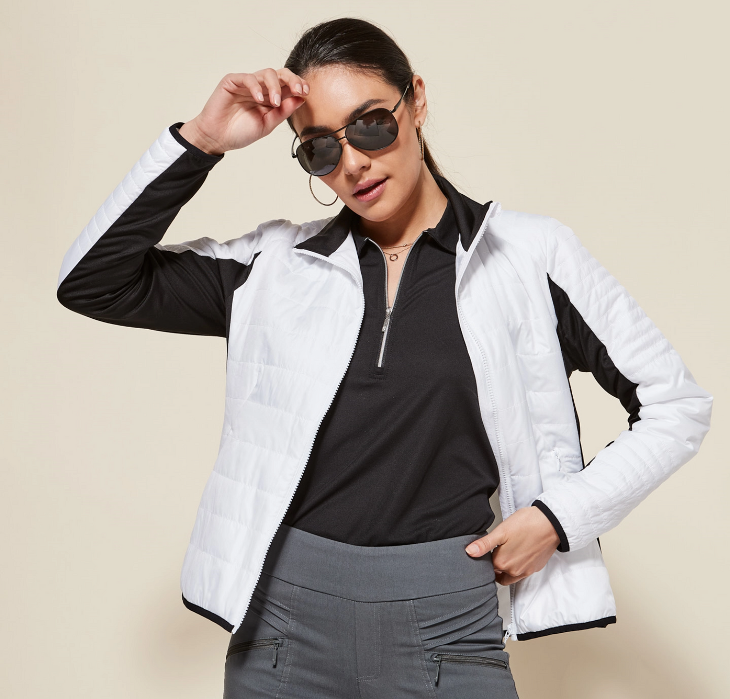Model posing in sunglasses, black top, gray golf pants, and white jacket